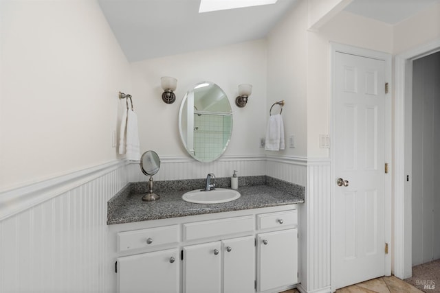 bathroom with a skylight, a wainscoted wall, walk in shower, and vanity