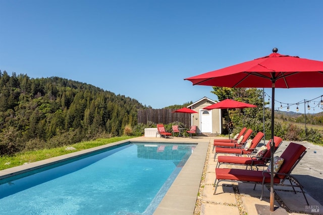 pool with a patio area, fence, and a wooded view