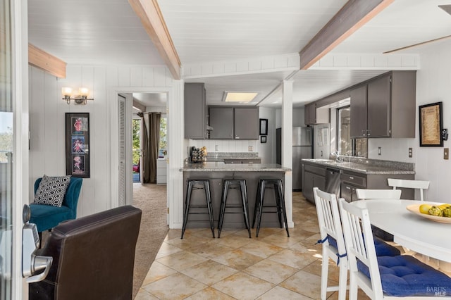 kitchen featuring a kitchen breakfast bar, appliances with stainless steel finishes, beam ceiling, gray cabinetry, and a peninsula