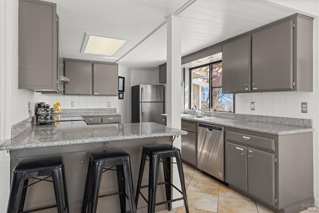 kitchen featuring a peninsula, a kitchen breakfast bar, gray cabinetry, and stainless steel appliances