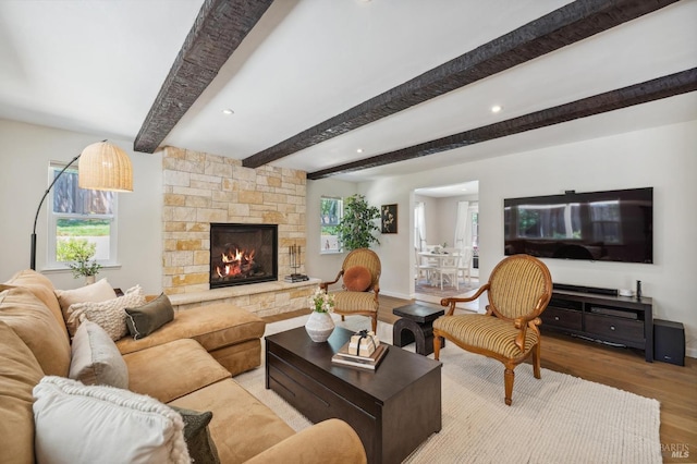 living area with beamed ceiling, baseboards, wood finished floors, recessed lighting, and a stone fireplace