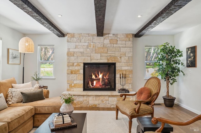 living room featuring a stone fireplace, baseboards, wood finished floors, and beam ceiling