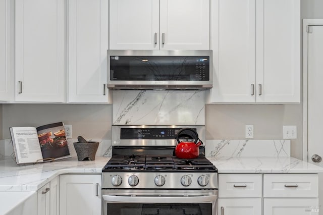 kitchen with white cabinets, decorative backsplash, light stone countertops, and stainless steel appliances