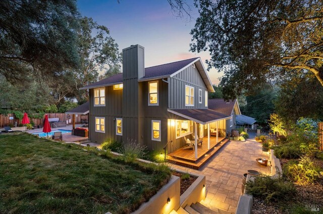back of property with board and batten siding, a patio area, fence, and a chimney