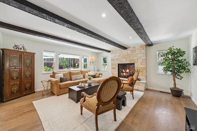 living room featuring baseboards, visible vents, beam ceiling, and light wood finished floors