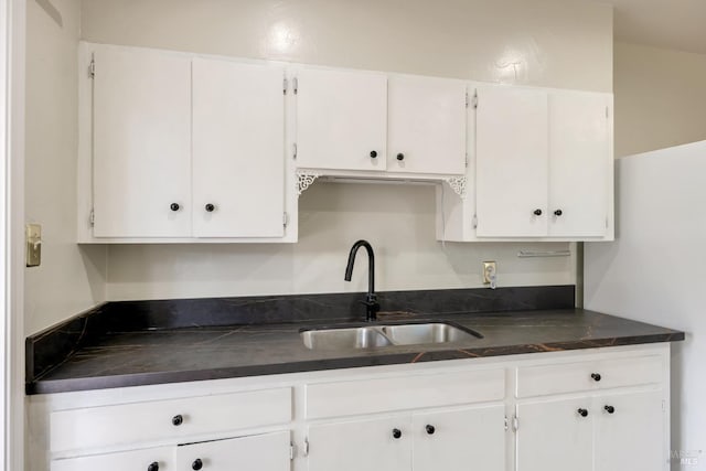 kitchen with white cabinetry, dark countertops, and a sink