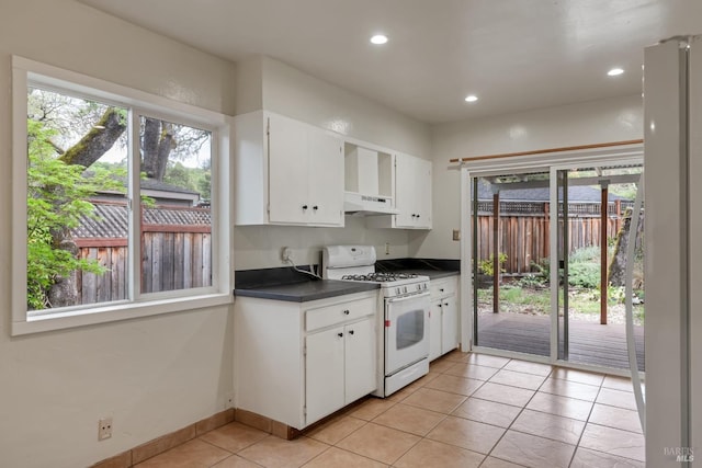 kitchen with dark countertops, white range with gas cooktop, white cabinetry, under cabinet range hood, and light tile patterned floors