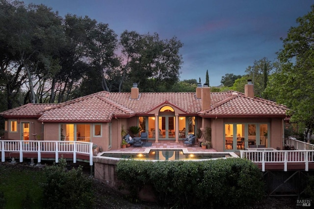rear view of property featuring an outdoor pool, stucco siding, french doors, a tiled roof, and a chimney