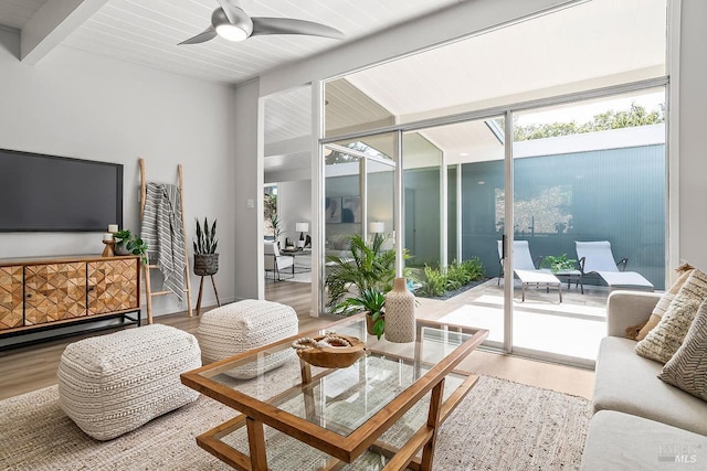 living area featuring wood finished floors, beam ceiling, a wall of windows, and ceiling fan