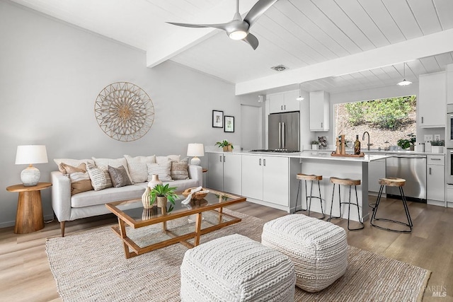 living area with ceiling fan, visible vents, wood finished floors, and beam ceiling