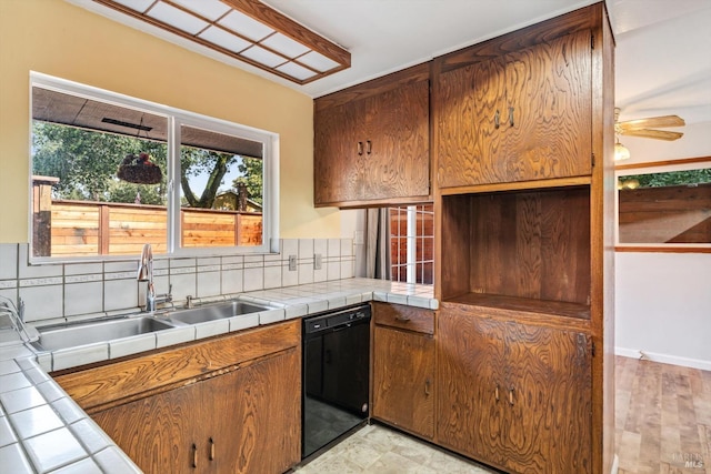 kitchen featuring brown cabinetry, tile countertops, tasteful backsplash, a sink, and black dishwasher