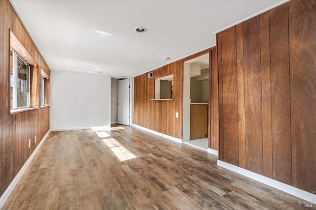 empty room featuring wooden walls, baseboards, and wood finished floors