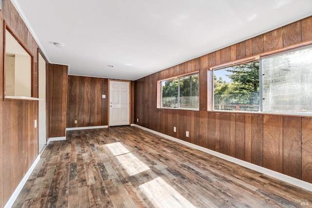empty room featuring baseboards, wood-type flooring, and wood walls
