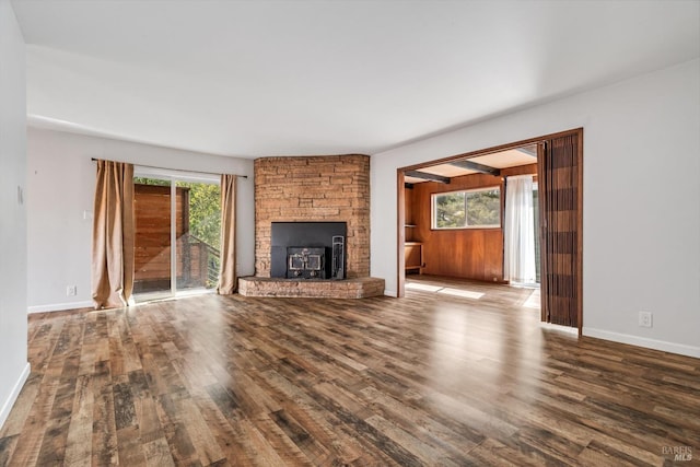 unfurnished living room featuring baseboards, a stone fireplace, and wood finished floors