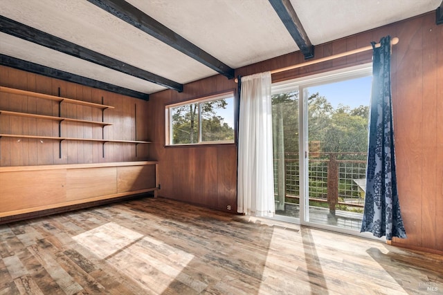 spare room featuring wood walls, hardwood / wood-style flooring, and beamed ceiling