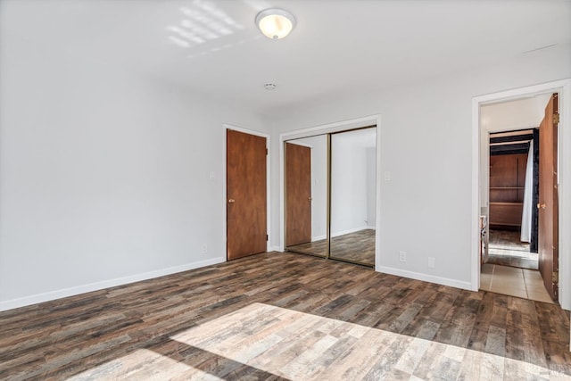 unfurnished bedroom featuring baseboards, wood finished floors, and a closet