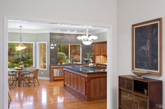 kitchen with light wood-type flooring, ornamental molding, a sink, dark countertops, and stainless steel gas stovetop
