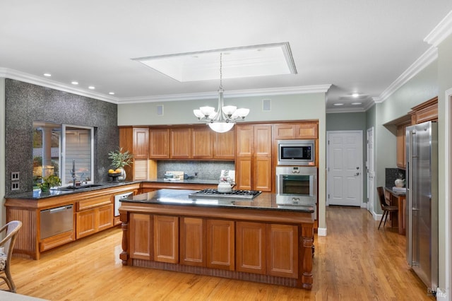 kitchen with brown cabinets, appliances with stainless steel finishes, a sink, light wood-type flooring, and an inviting chandelier