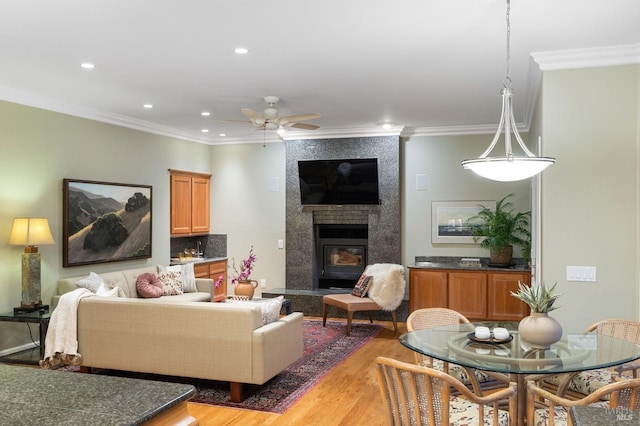 living area with a ceiling fan, a fireplace, light wood-type flooring, ornamental molding, and recessed lighting