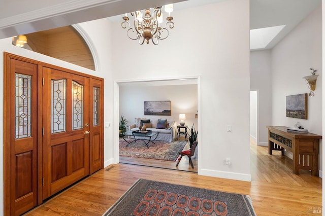 foyer featuring a high ceiling, baseboards, light wood-style flooring, and an inviting chandelier