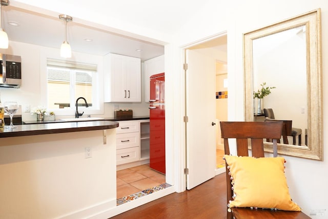 kitchen featuring white cabinets, stainless steel microwave, a sink, dark countertops, and light wood finished floors