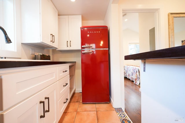 kitchen with light tile patterned flooring, freestanding refrigerator, dark countertops, and white cabinetry