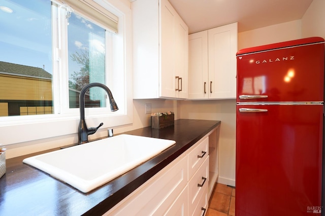 kitchen with light tile patterned floors, a sink, freestanding refrigerator, dark countertops, and white cabinetry