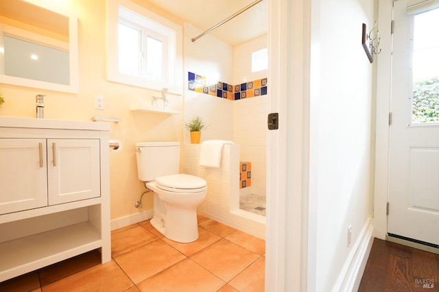 bathroom featuring tiled shower, vanity, tile patterned flooring, toilet, and baseboards