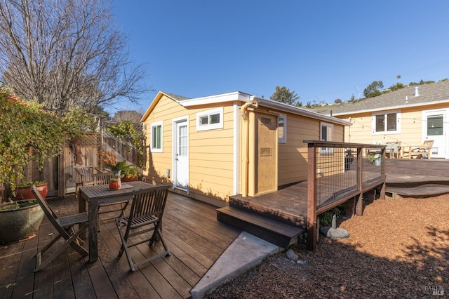 wooden terrace featuring outdoor dining area, an outdoor structure, and fence
