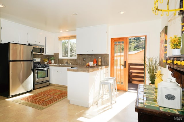 kitchen with a kitchen breakfast bar, tasteful backsplash, white cabinets, a sink, and stainless steel appliances