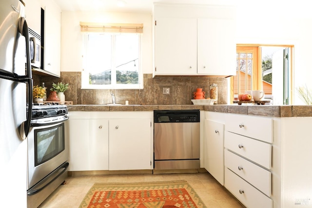 kitchen with a peninsula, tile counters, white cabinetry, stainless steel appliances, and backsplash