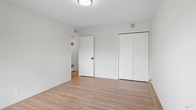 unfurnished bedroom with light wood-type flooring, visible vents, and a closet