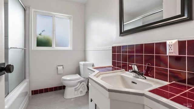full bath with bath / shower combo with glass door, toilet, baseboards, tile patterned flooring, and vanity