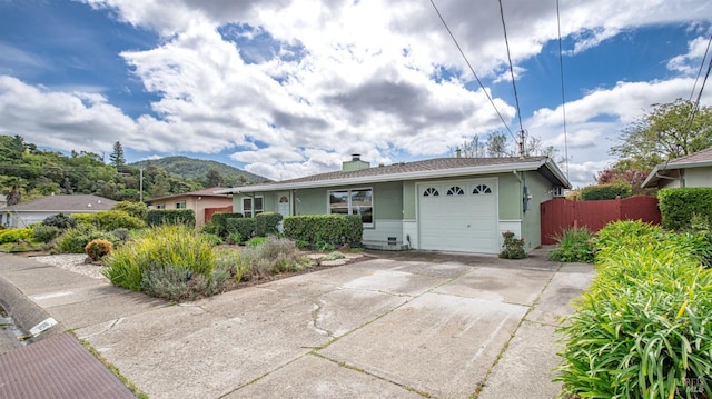 ranch-style home featuring a mountain view, driveway, fence, a garage, and stucco siding