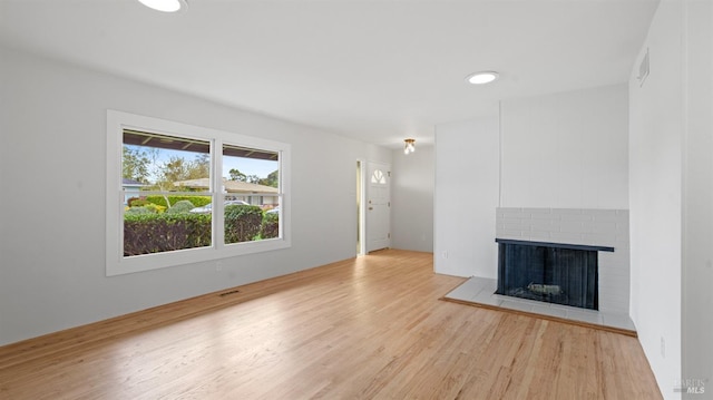 unfurnished living room with visible vents, light wood-style flooring, and a brick fireplace