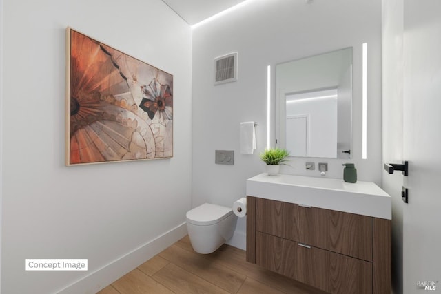 bathroom featuring visible vents, baseboards, toilet, wood finished floors, and vanity