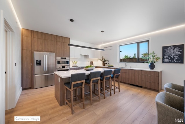 kitchen with stainless steel appliances, a breakfast bar, a sink, light wood-style floors, and modern cabinets