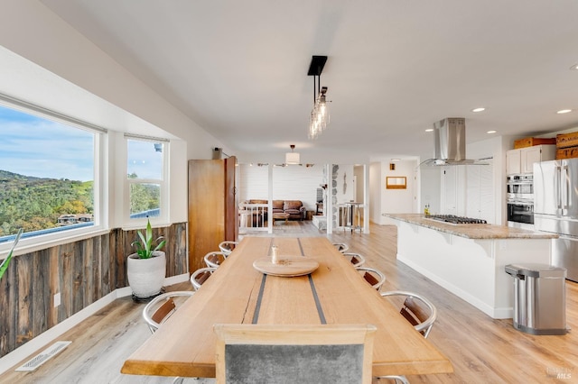 dining area featuring light wood finished floors, baseboards, visible vents, recessed lighting, and wood walls