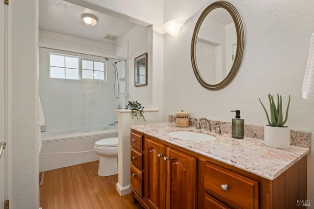 bathroom with visible vents, combined bath / shower with glass door, wood finished floors, toilet, and vanity
