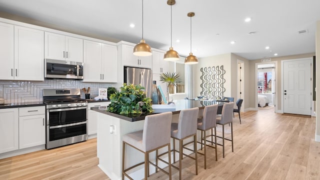 1096 Fiano Pl, Manteca, CA 95337 - kitchen featuring appliances with stainless steel finishes, dark countertops, a center island, backsplash, and light wood finished floors