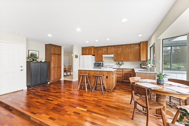 kitchen with a center island, under cabinet range hood, white appliances, and wood finished floors
