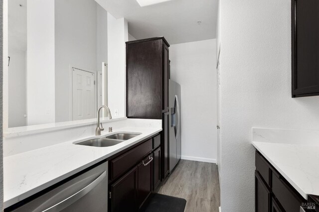kitchen featuring light stone countertops, a sink, stainless steel appliances, light wood-style flooring, and dark brown cabinets
