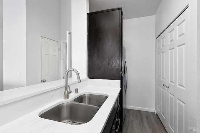 kitchen featuring dark wood-type flooring, light stone countertops, baseboards, and a sink