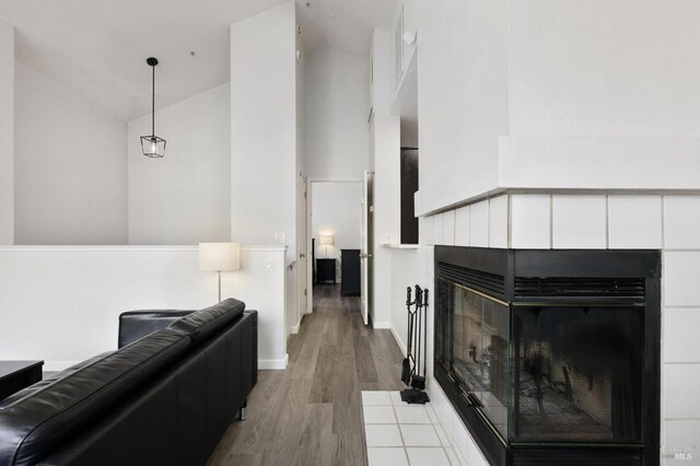 living area featuring a tile fireplace, high vaulted ceiling, wood finished floors, and baseboards