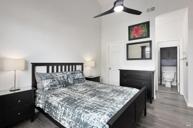 bedroom with wood finished floors, ensuite bathroom, baseboards, visible vents, and a high ceiling