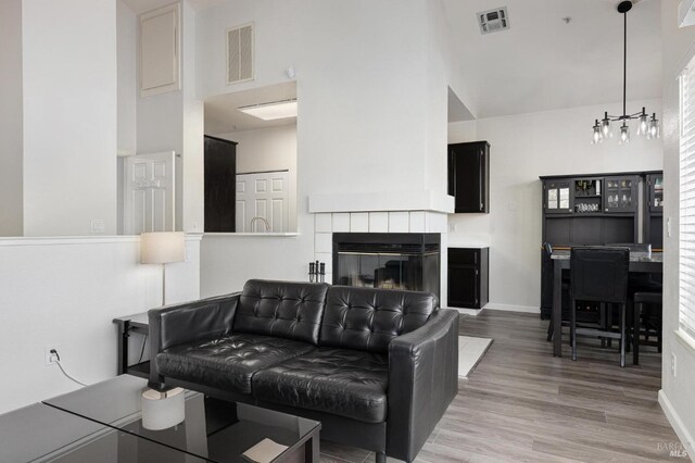 living area with wood finished floors, visible vents, a tile fireplace, and a high ceiling