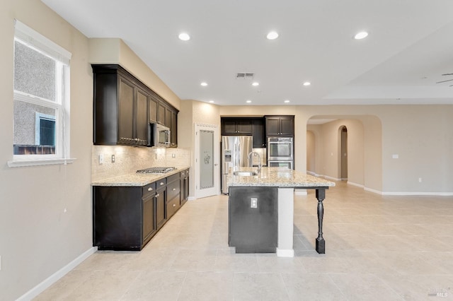 8568 Pinehollow Cir, Discovery Bay, CA 94505 - kitchen featuring appliances with stainless steel finishes, arched walkways, a kitchen island with sink, a breakfast bar, and light stone counters