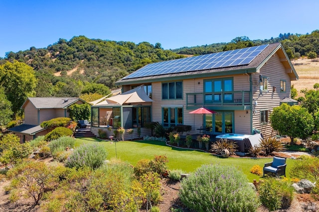 rear view of property with a yard, a hot tub, and roof mounted solar panels