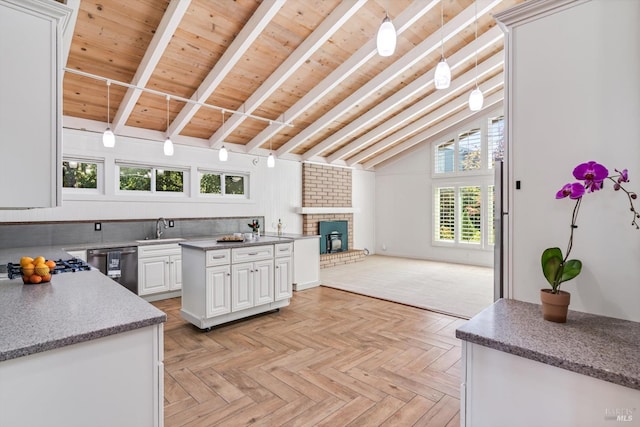 kitchen featuring white cabinetry, open floor plan, lofted ceiling with beams, a sink, and a brick fireplace