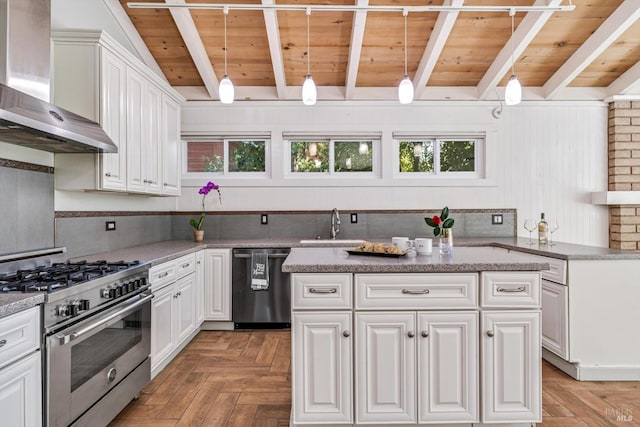 kitchen featuring a sink, beam ceiling, white cabinets, appliances with stainless steel finishes, and wall chimney exhaust hood